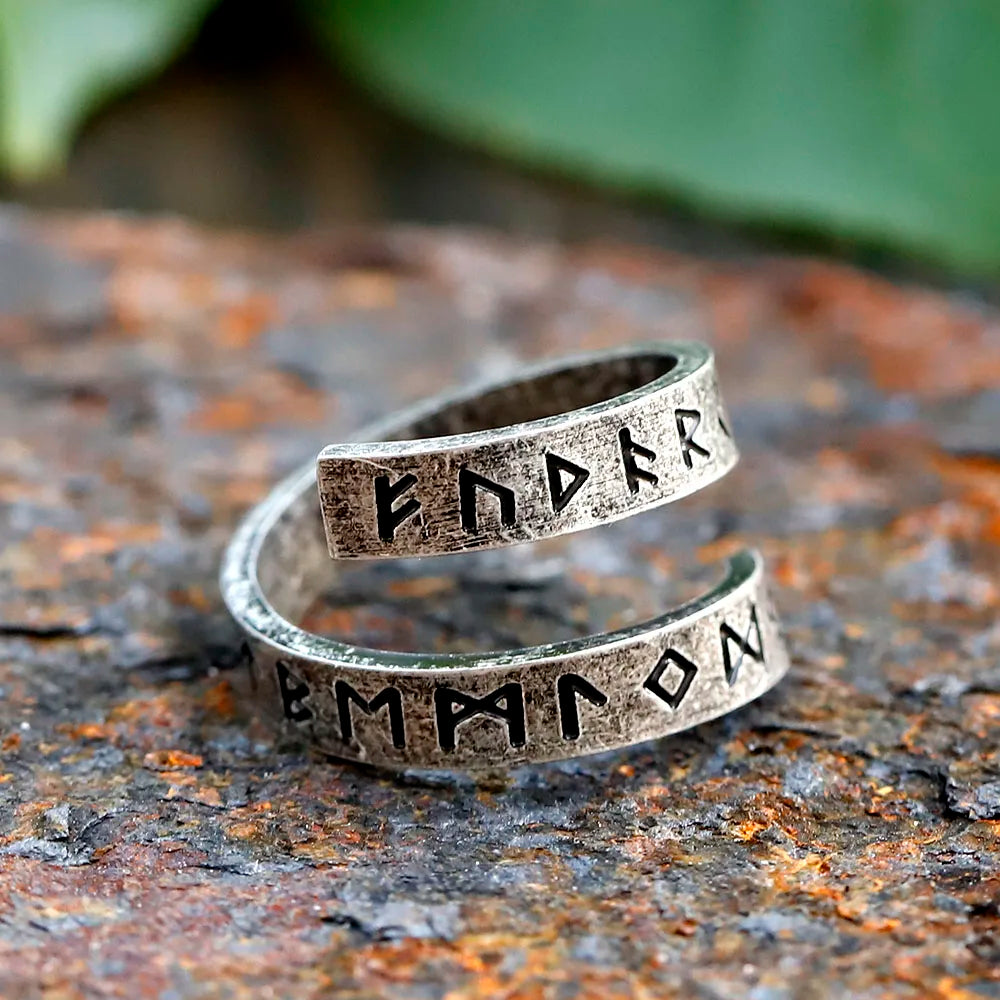 silver ring with engraved text on a textured surface with green leaves in the background