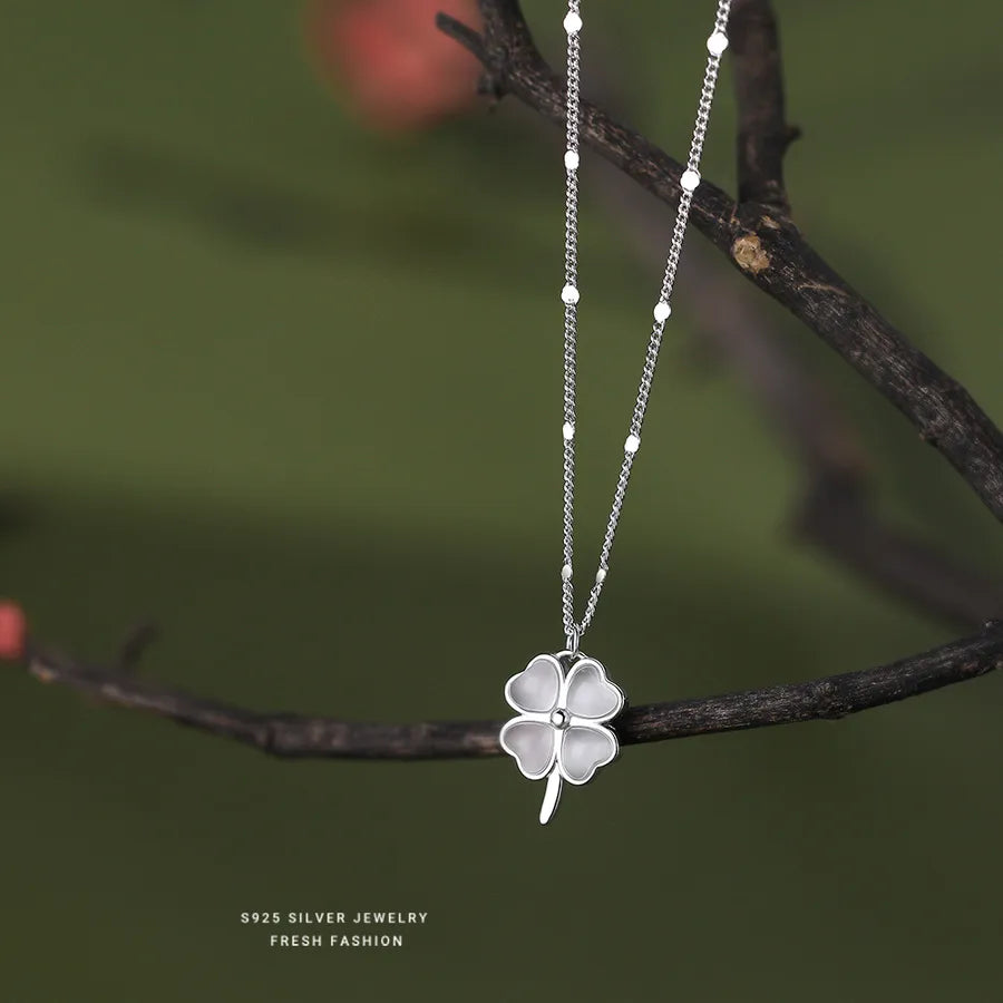 Silver four-leaf clover necklace displayed on branch
