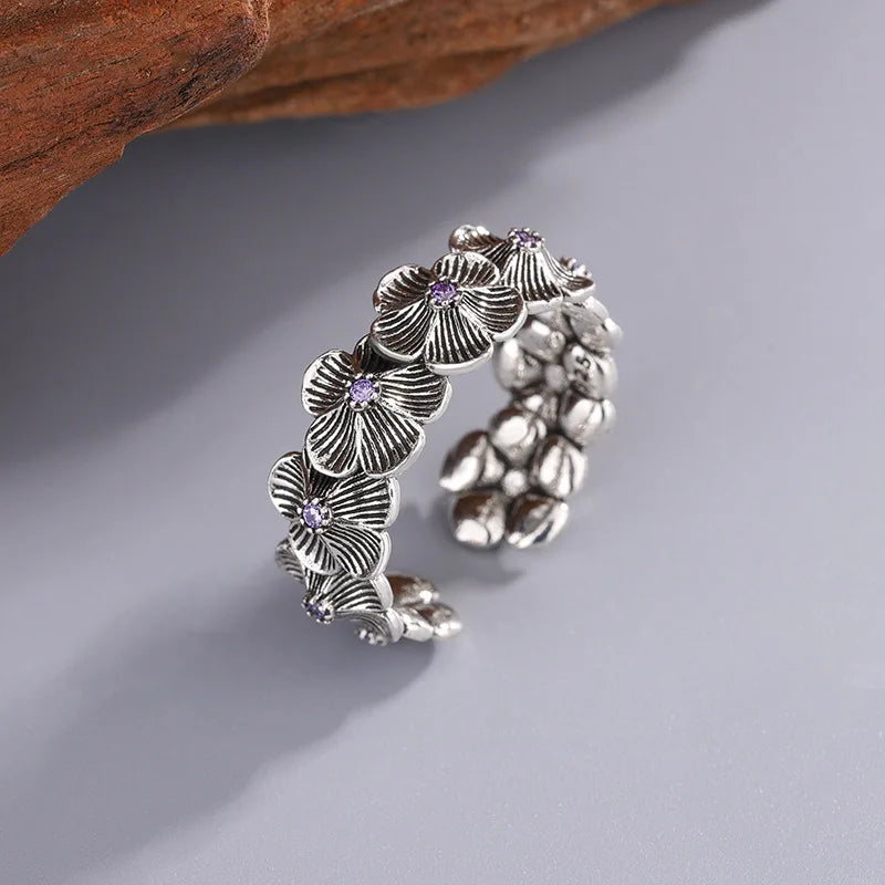Close-up of a 925 sterling silver flower ring with detailed petals and purple zircon stones on a gray surface