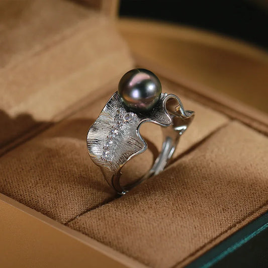 Side view of silver-tone wave ring with black imitation pearl and crystal detailing in velvet jewelry box