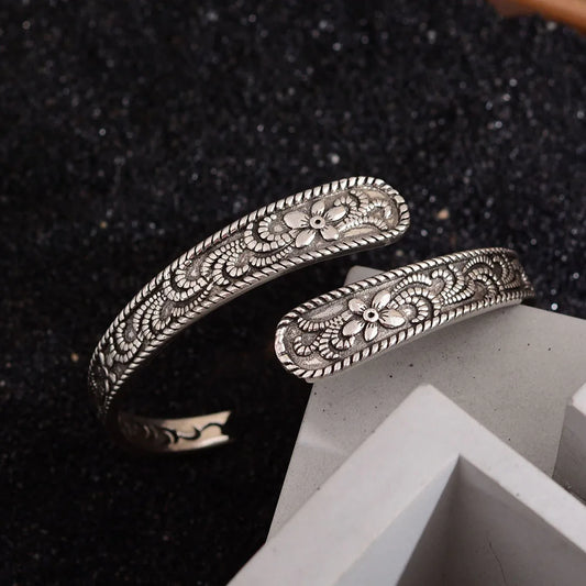 Antiqued silver-plated open cuff bracelet with intricate floral design on dark and light props