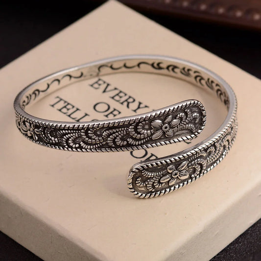 Silver-plated vintage cuff bracelet with floral engraving, displayed on a book background